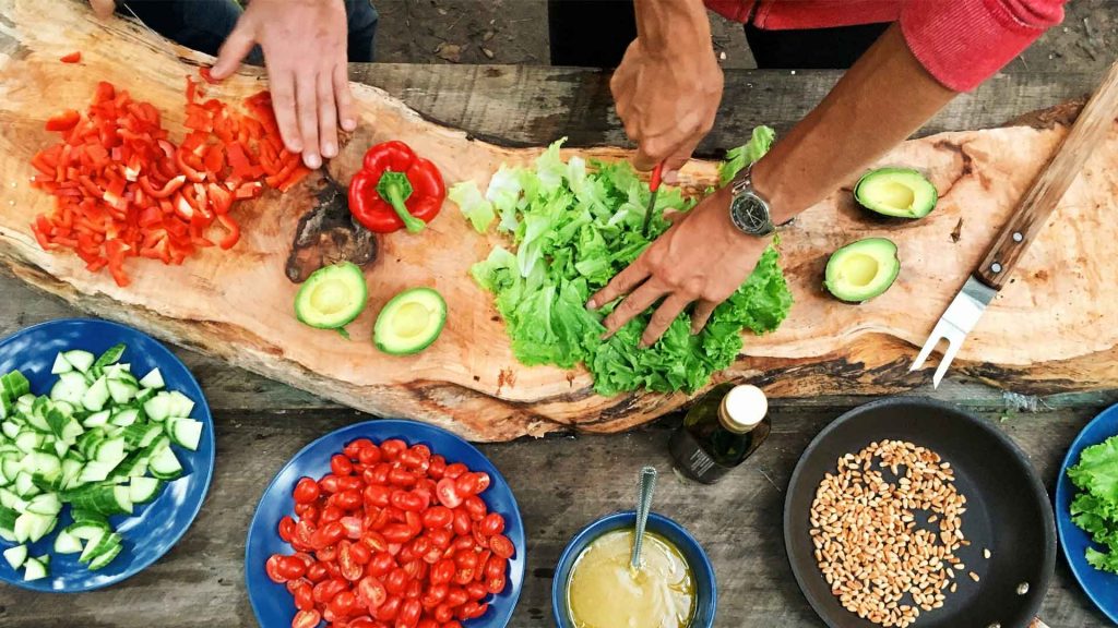 Two people prep a meal by chopping vegetables on a block of wood.