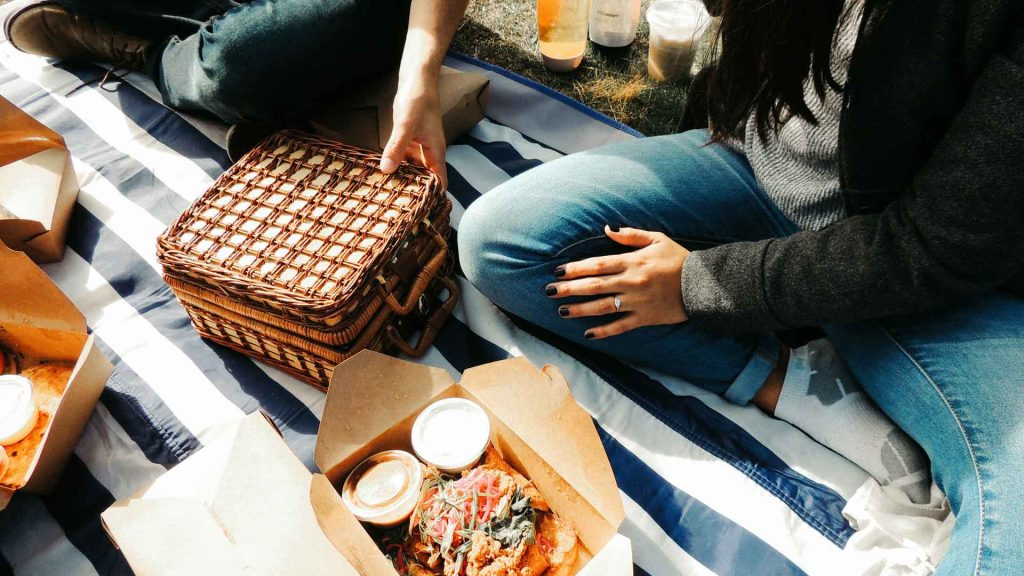 Two people have a picnic on a blue and white striped blanket.