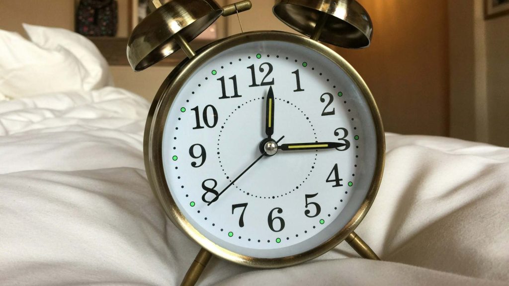 A brass alarm clock placed on a white duvet.
